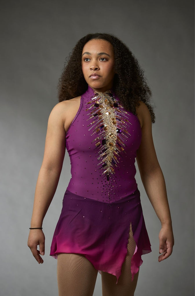 One-of-a-kind purple figure skating competition dress with asymmetrical chiffon skirt, high-neck sleeveless bodice, and crystal embellishments, model Miranda, closeup front view – Elite Xpression
Robe unique de compétition de patinage artistique avec jupe en chiffon asymétrique, corsage sans manches à col montant et ornements en cristaux, modèle Miranda, vue rapprochée de face – Elite Xpression.